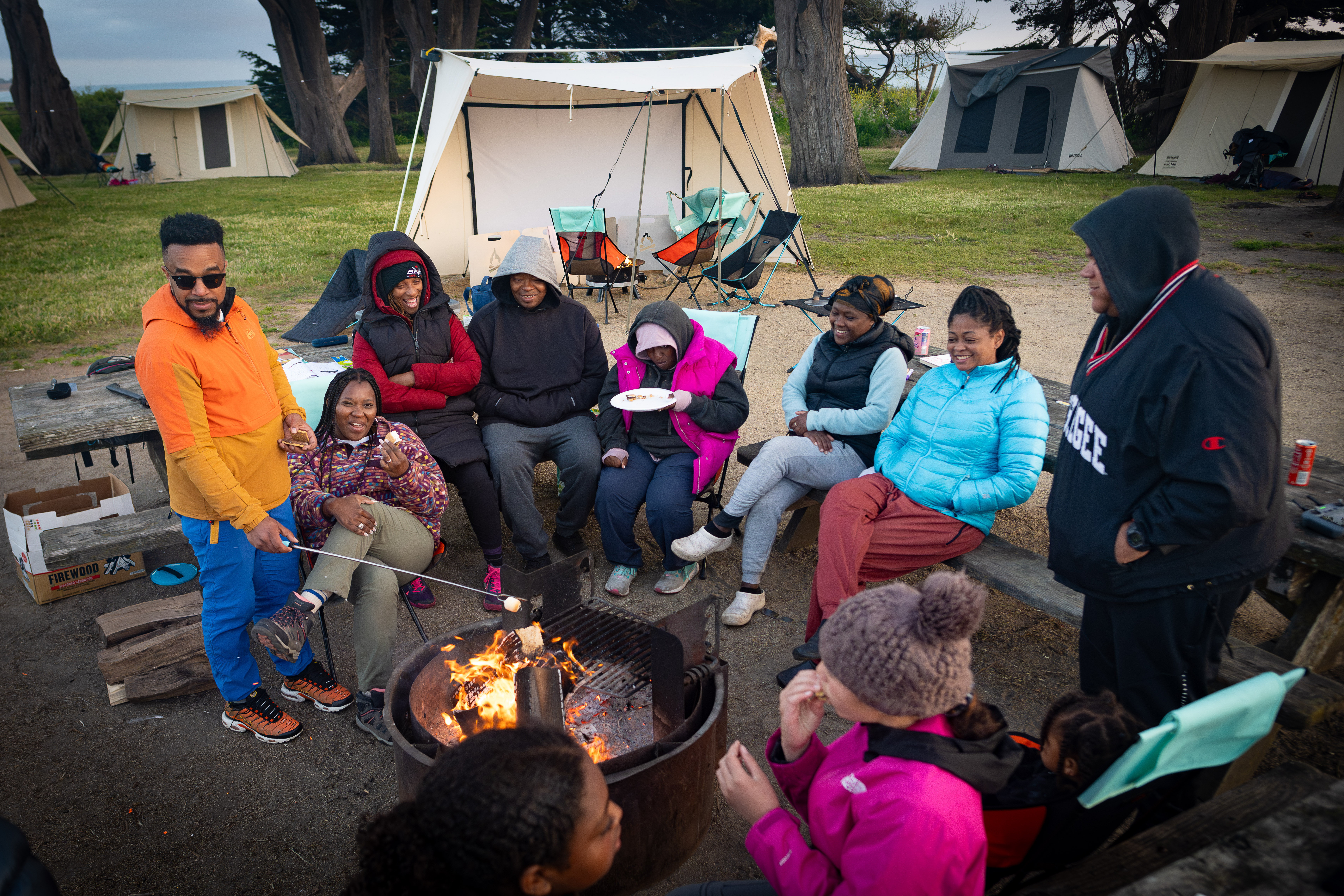 Family gathered around a campfire at a coastal campground at sunset