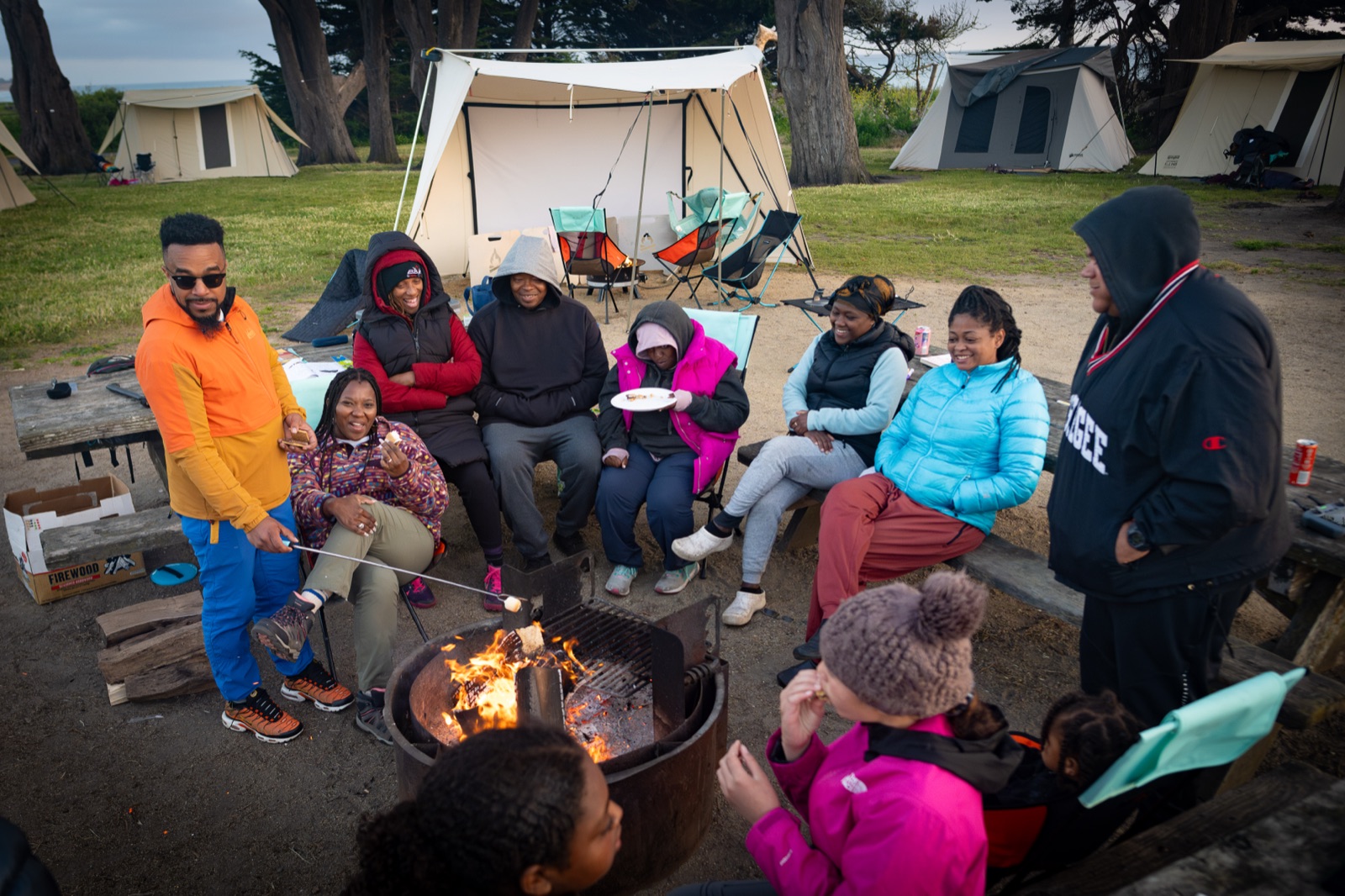 Family gathered around a campfire at a coastal campground at sunset