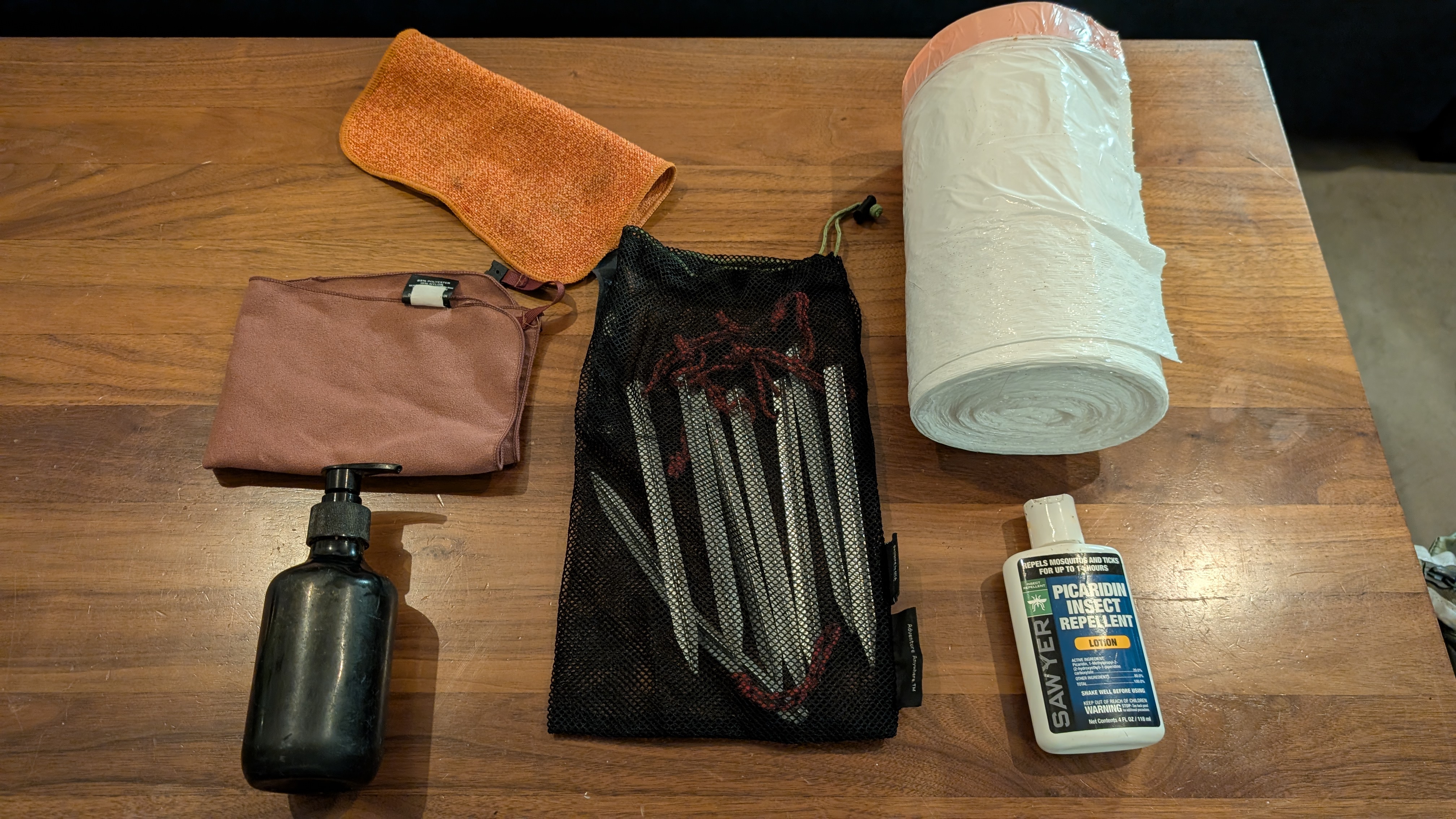 Collection of commonly forgotten camping items including trash bags, tent stakes, dish towels, soap, toilet paper, and bug spray