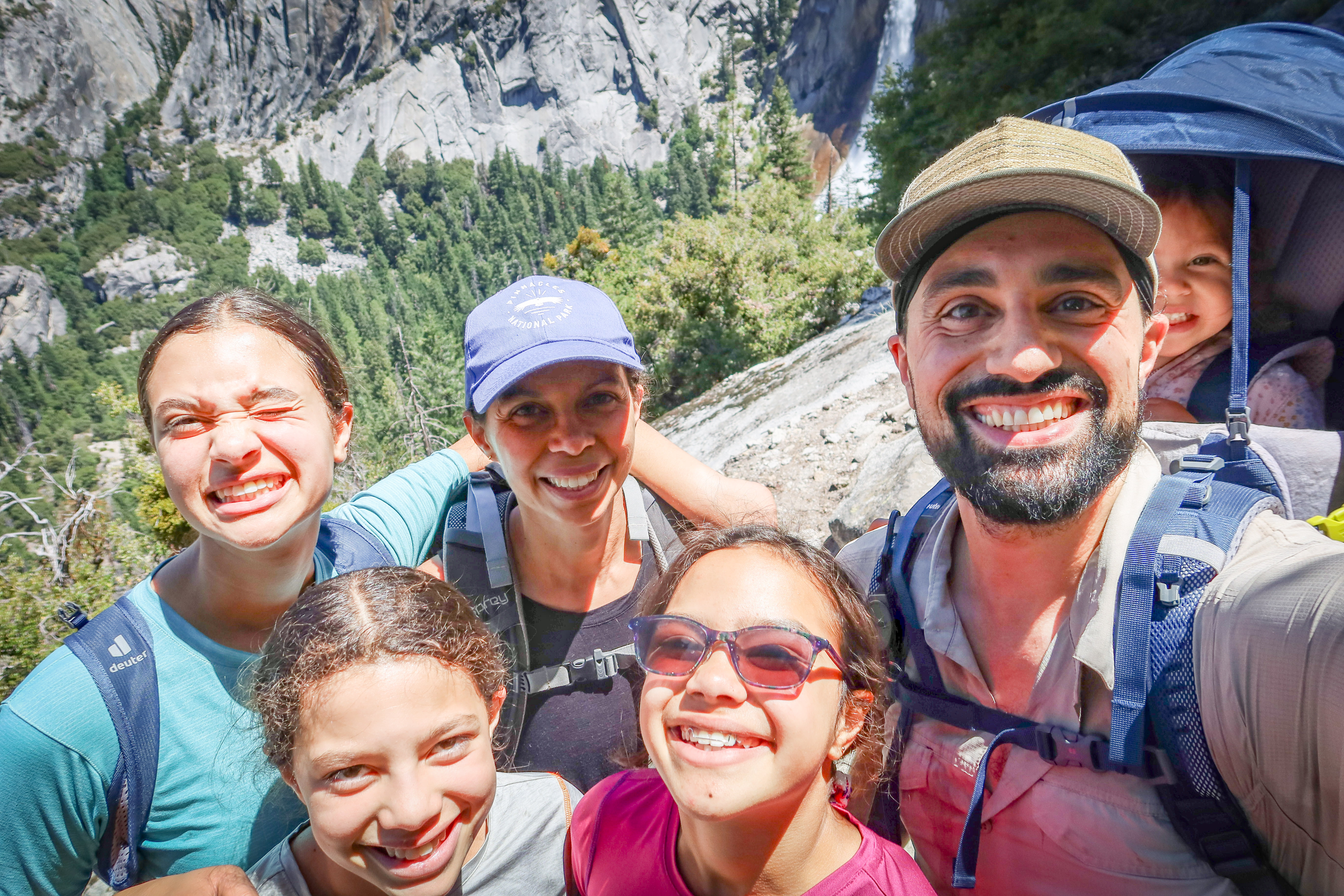 The Steele family on the Mist Trail in Yosemite National Park, August 2023. Mom Sally, dad Justin, three older daughters, and toddler in a child carrier. The Steele family on the Mist Trail in Yosemite National Park, August 2023. Mom Sally, dad Justin, three older daughters, and toddler in a child carrier.