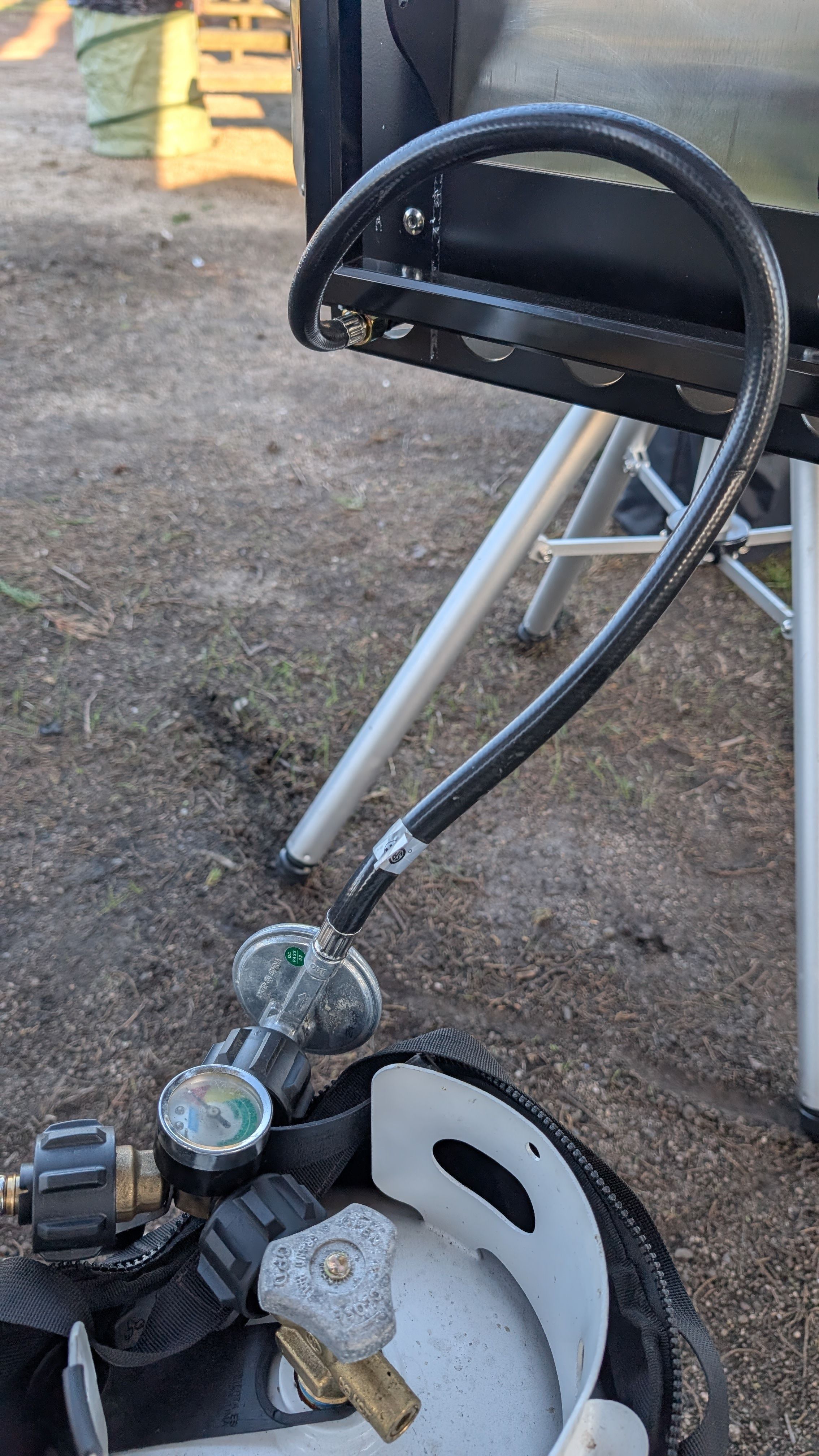Close-up of propane gas line connection at back of grill with regulator and pressure gauge