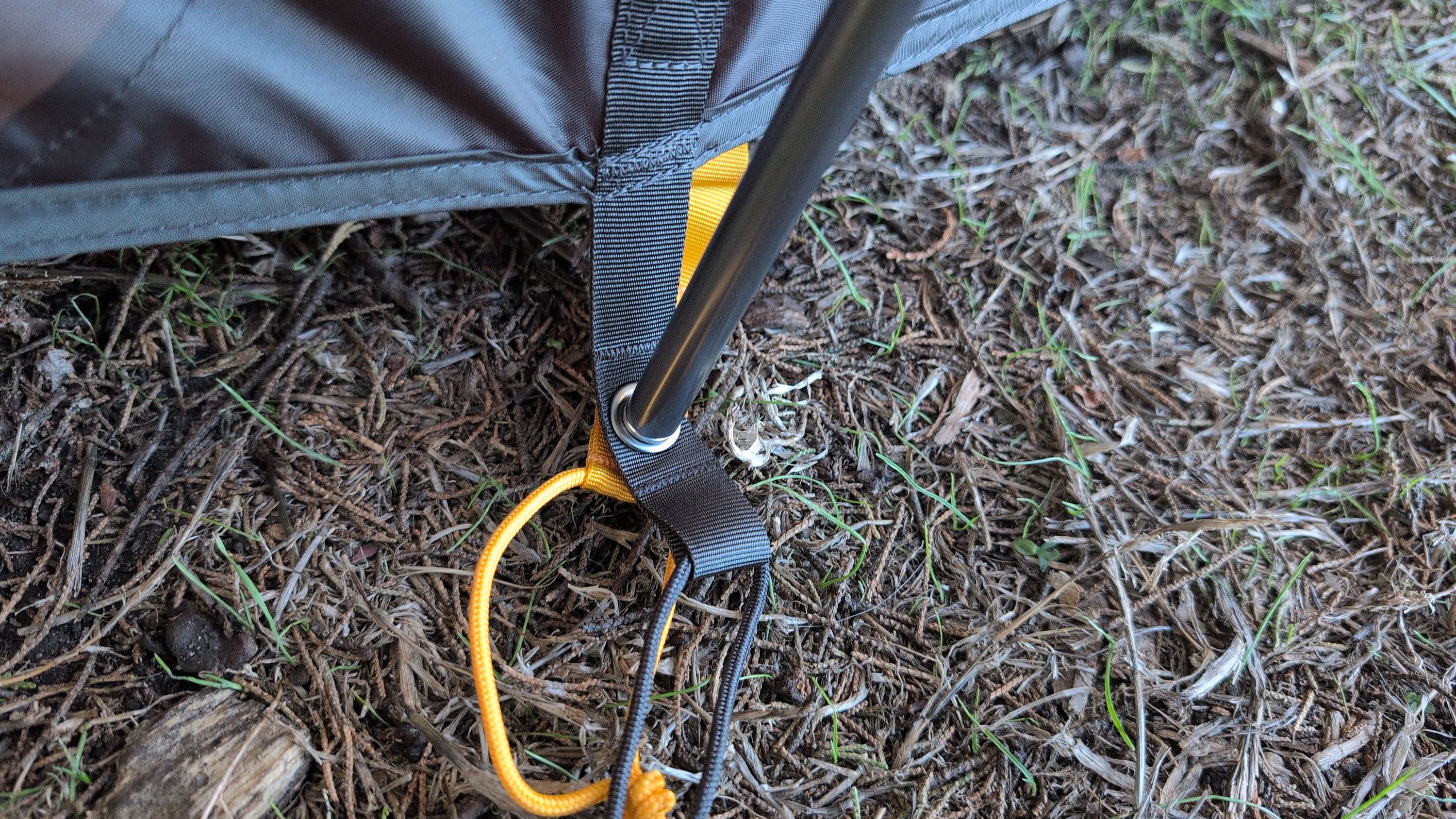 Close-up of gray pole end going through tent and orange ground sheet grommet